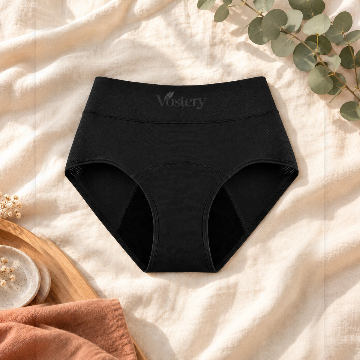 Culotte absorbante Vostery noire taille haute posée à plat sur du lin