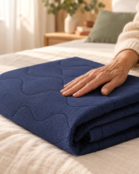 Gros plan du drap protège-matelas matelassé bleu marine, main posée sur le tissu doux
